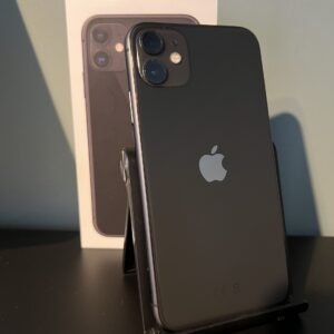 Refurbished iPhone 11 128 GB zwart op standaard met originele verpakking op de achtergrond – dubbele camera en glanzende afwerking zichtbaar.